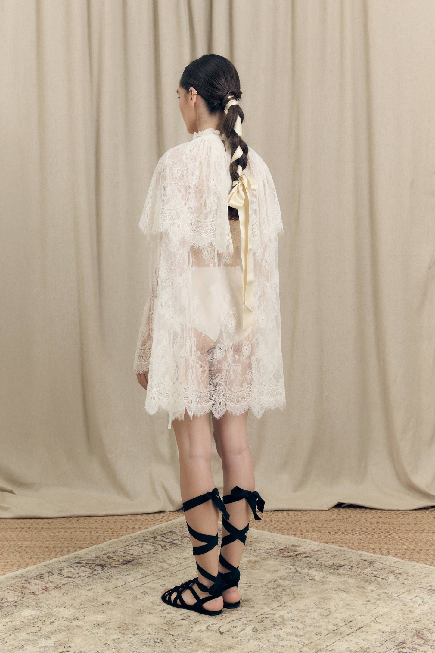 Model wearing Botteghe Oscure dress in French Chantilly lace with draped lace capelet and silk details – back view