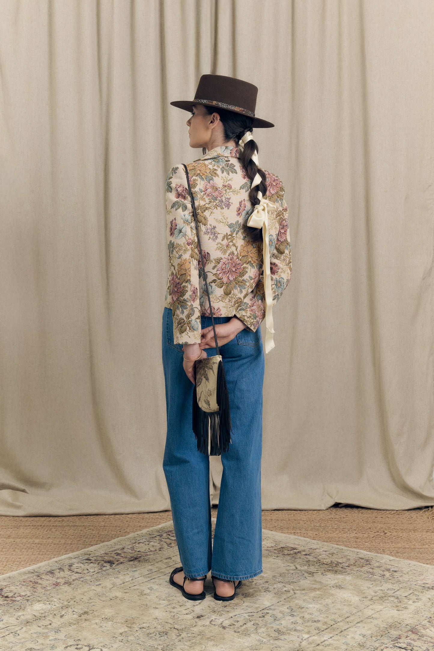 Back view of floral vintage jacquard blazer by Botteghe Oscure, boxy fit with tailored cut, styled with crossbody mini bag in tapestry fabric and leather fringes.