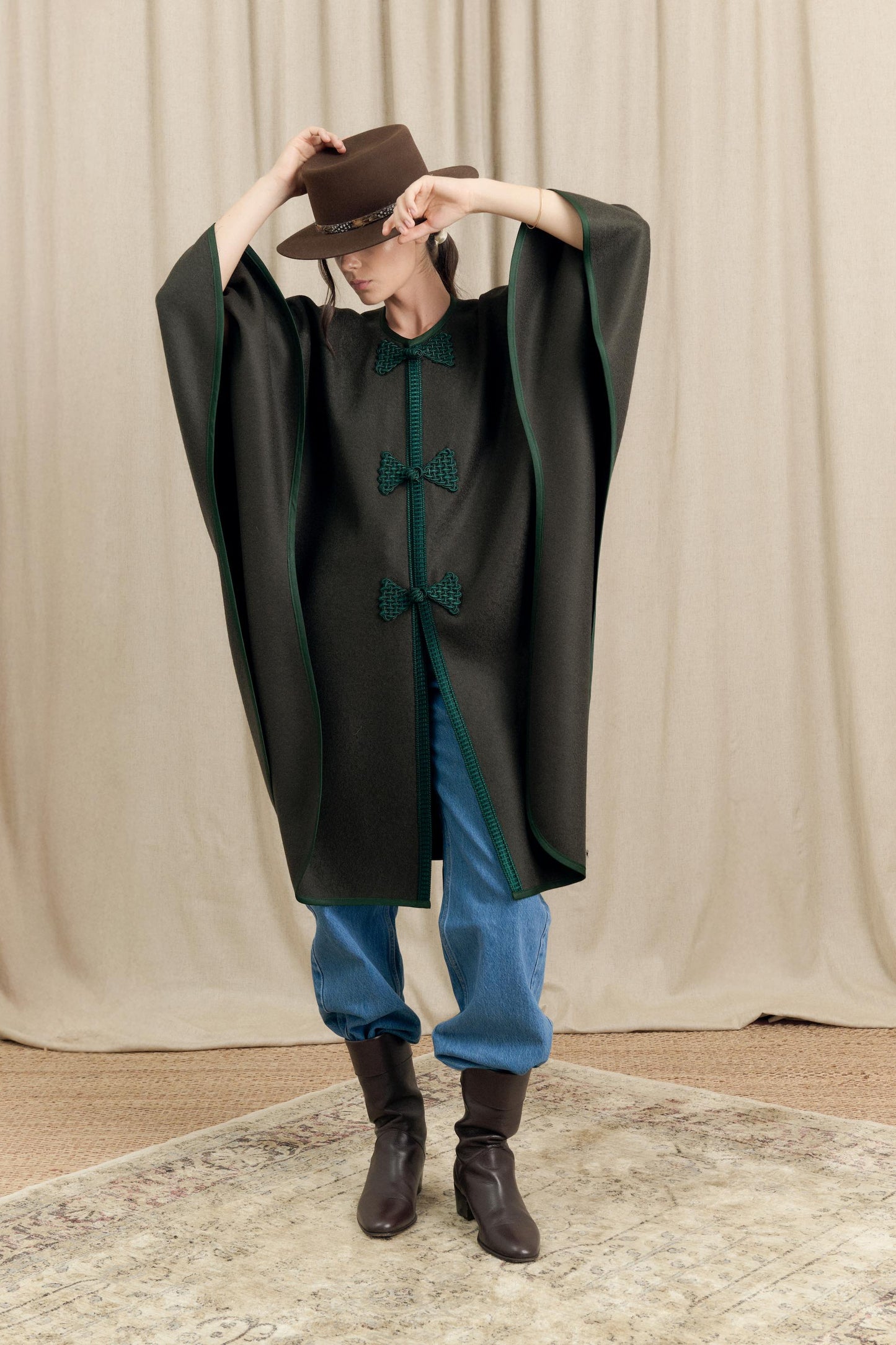 Model lifting arms wearing Botteghe Oscure Loden Cape, showing drape and volume