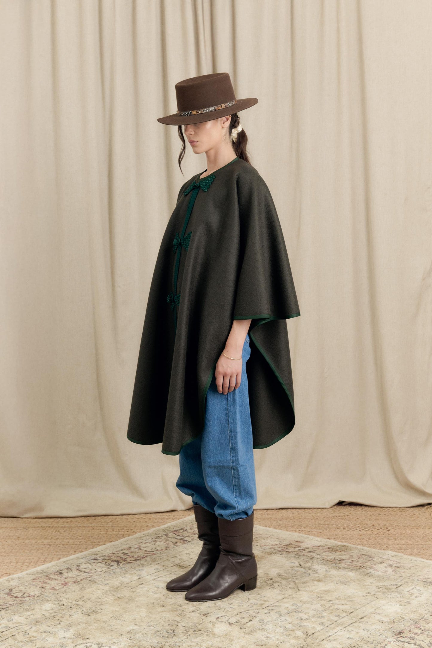 Side profile of model wearing Botteghe Oscure loden cape with gros-grain trim and handmade details