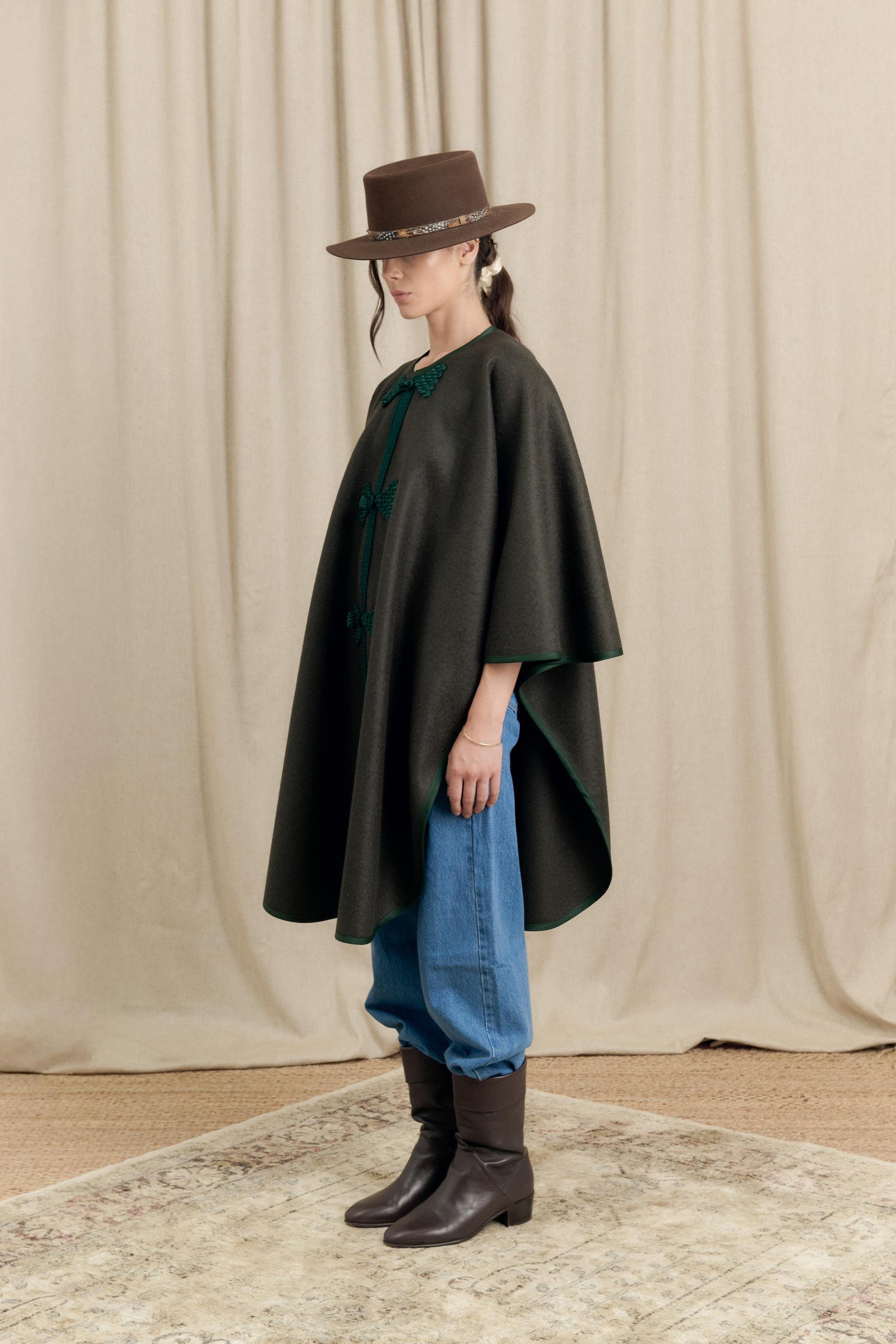 Side profile of model wearing Botteghe Oscure loden cape with gros-grain trim and handmade details