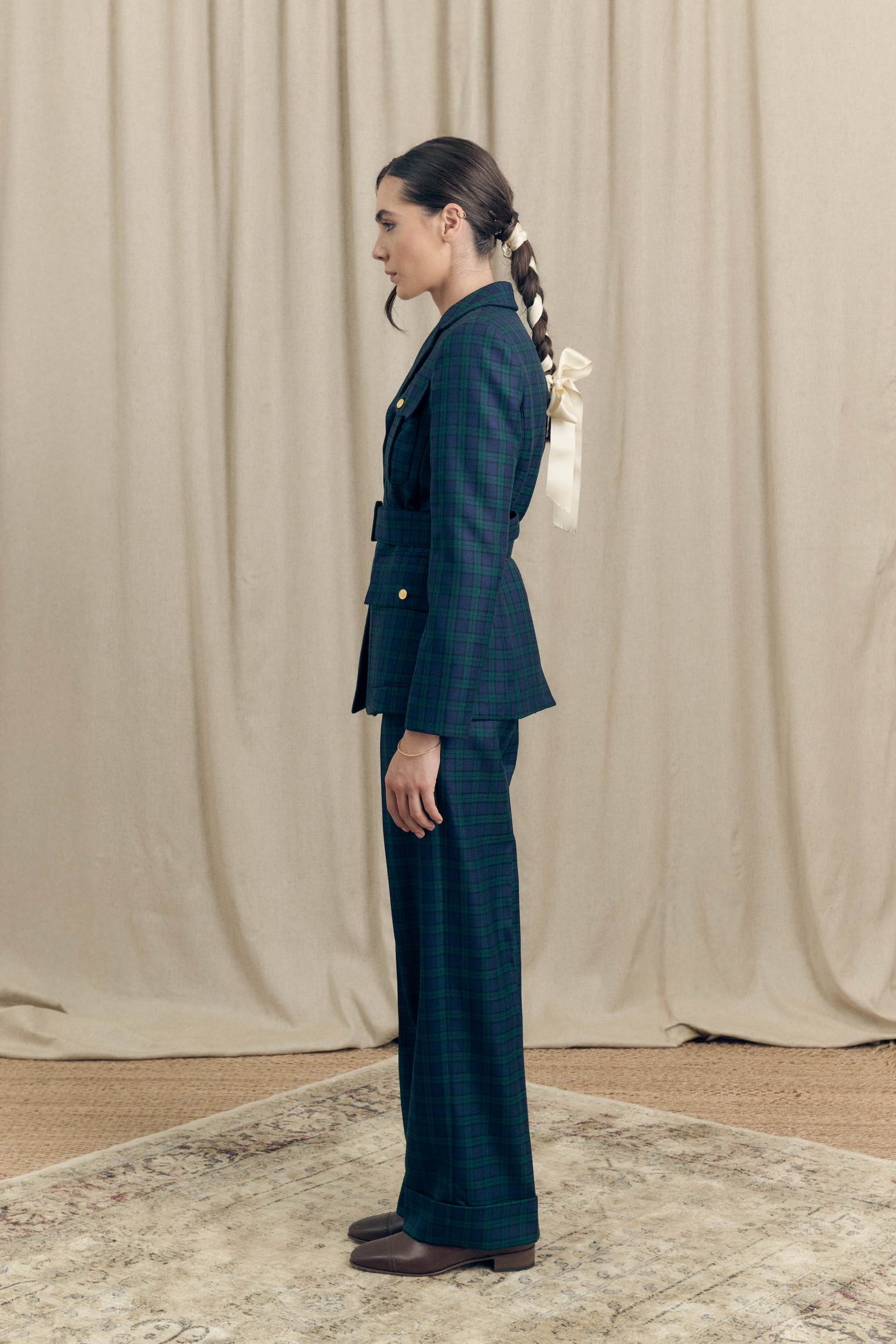 Side profile of model wearing belted military blazer and matching tartan trousers in Black Watch wool by Botteghe Oscure.