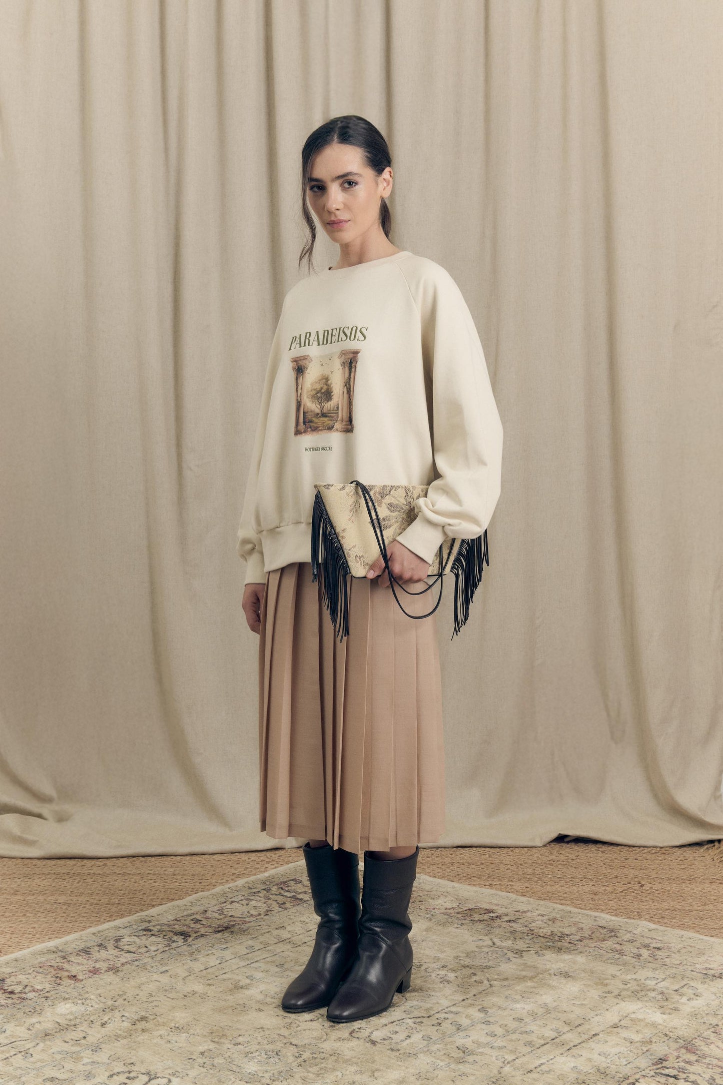 Front view of model wearing a pleated midi skirt in virgin wool paired with an oversized sweatshirt featuring Paradeisos drawing and embroidery.
