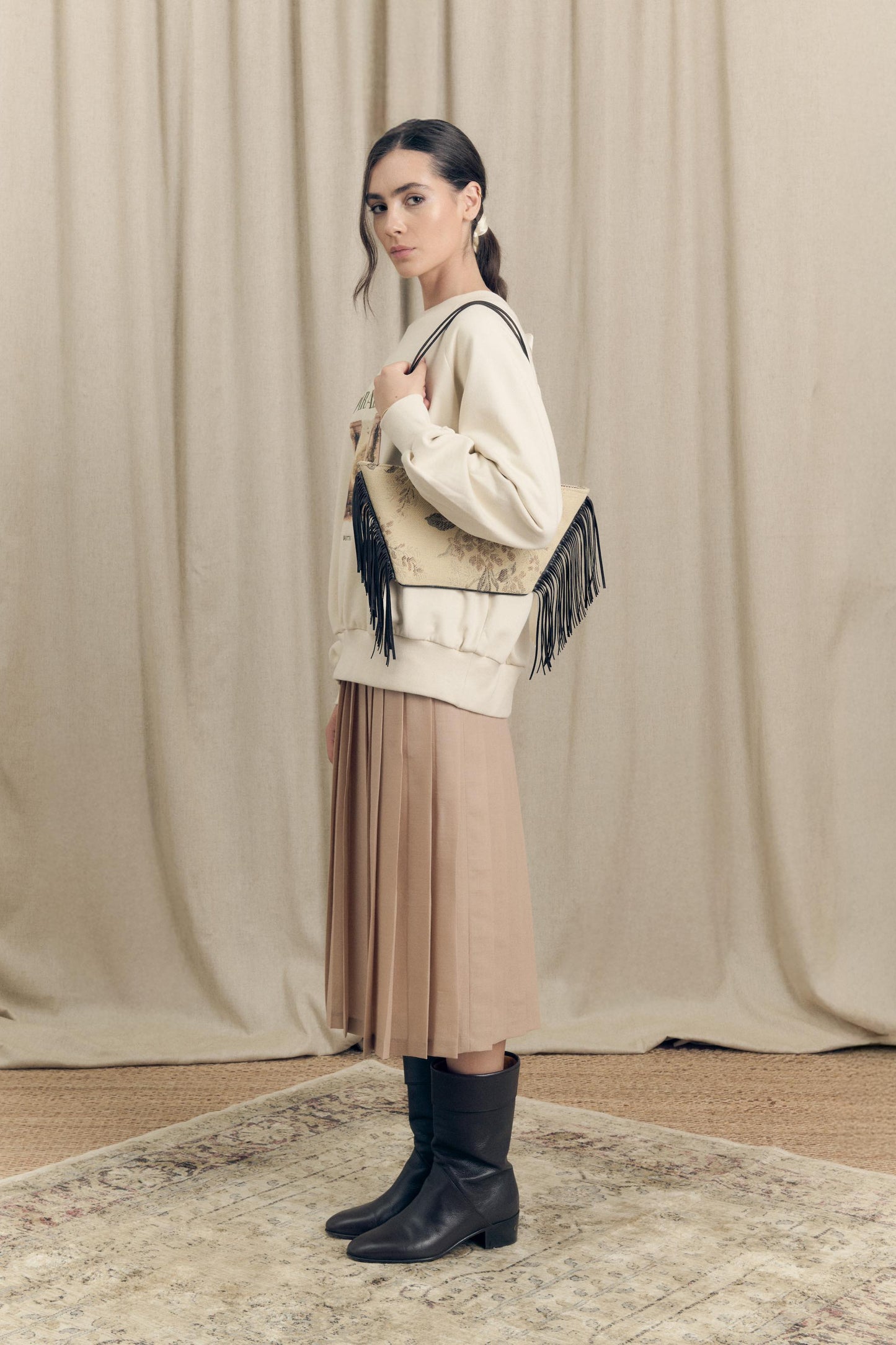 Side view of model wearing a pleated midi skirt in virgin wool paired with an oversized sweatshirt featuring Paradeisos drawing and embroidery.

