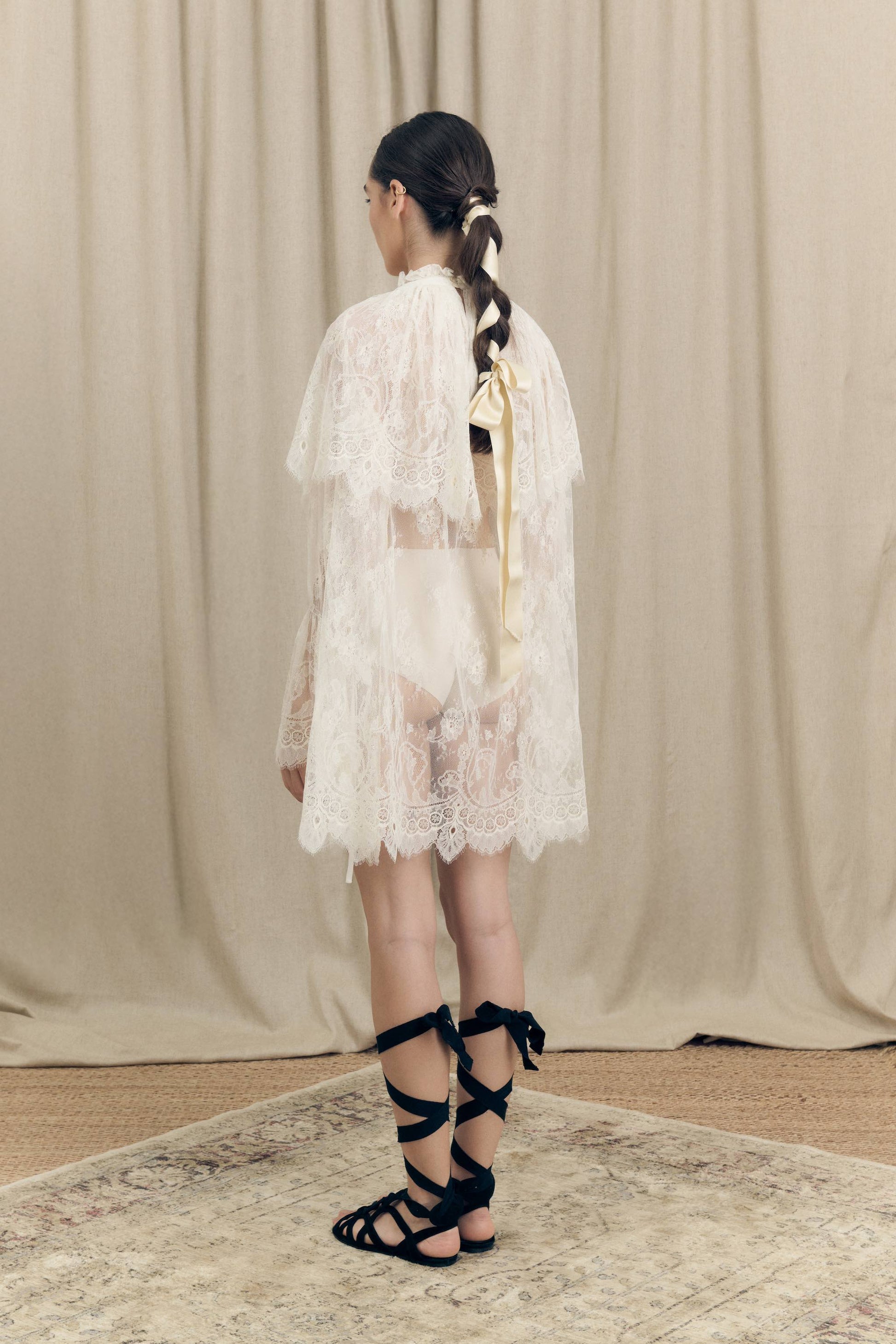 Model wearing Botteghe Oscure dress in French Chantilly lace with draped lace capelet and silk details – back view