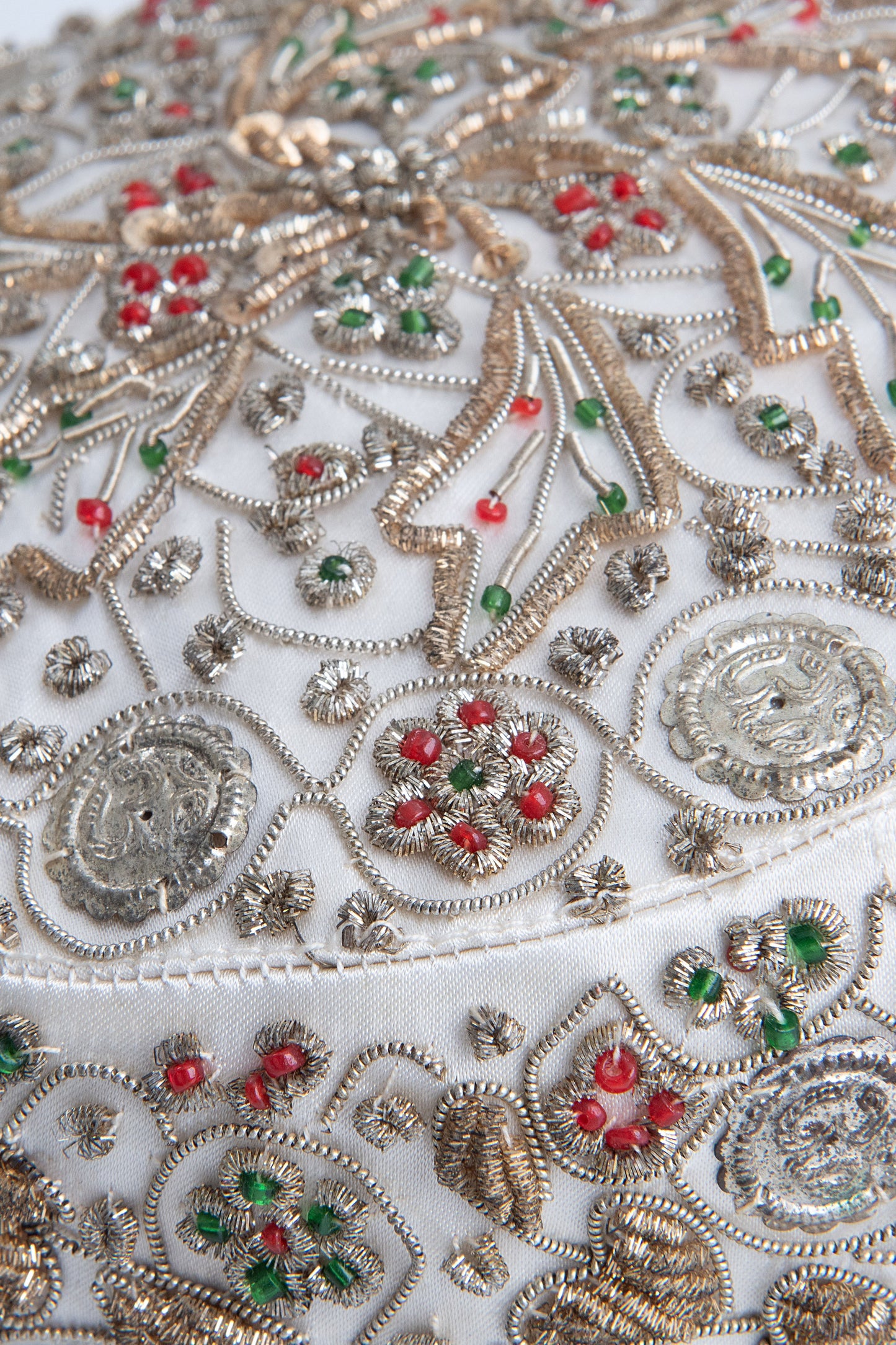 Close-up of hand-applied zardozi embroidery on vintage silk, showcasing intricate floral patterns, metallic coils and red and green glass beads.
