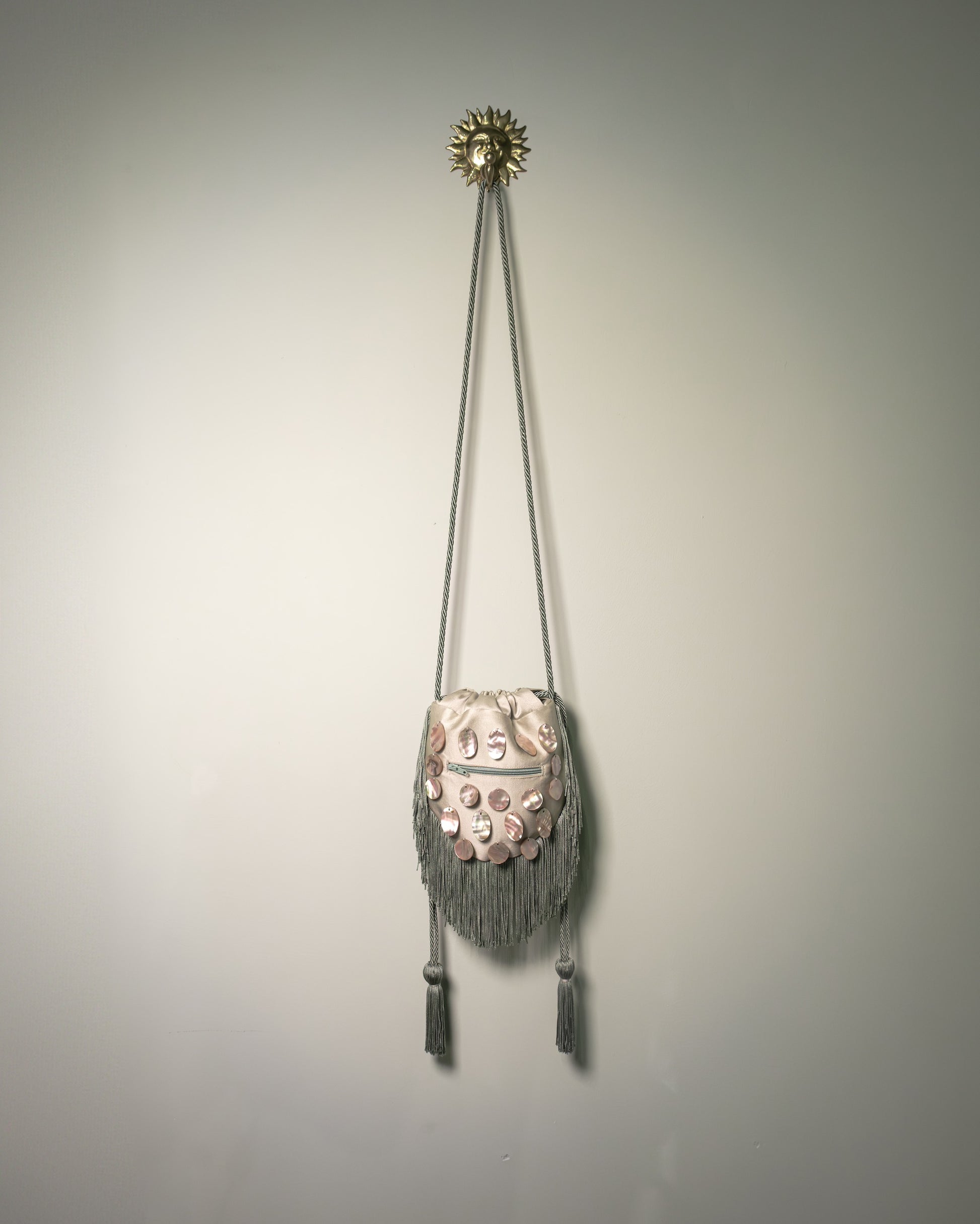 Back view of the sage green duchesse cotton reticule bag featuring a rear zip pocket and decorative fringe.