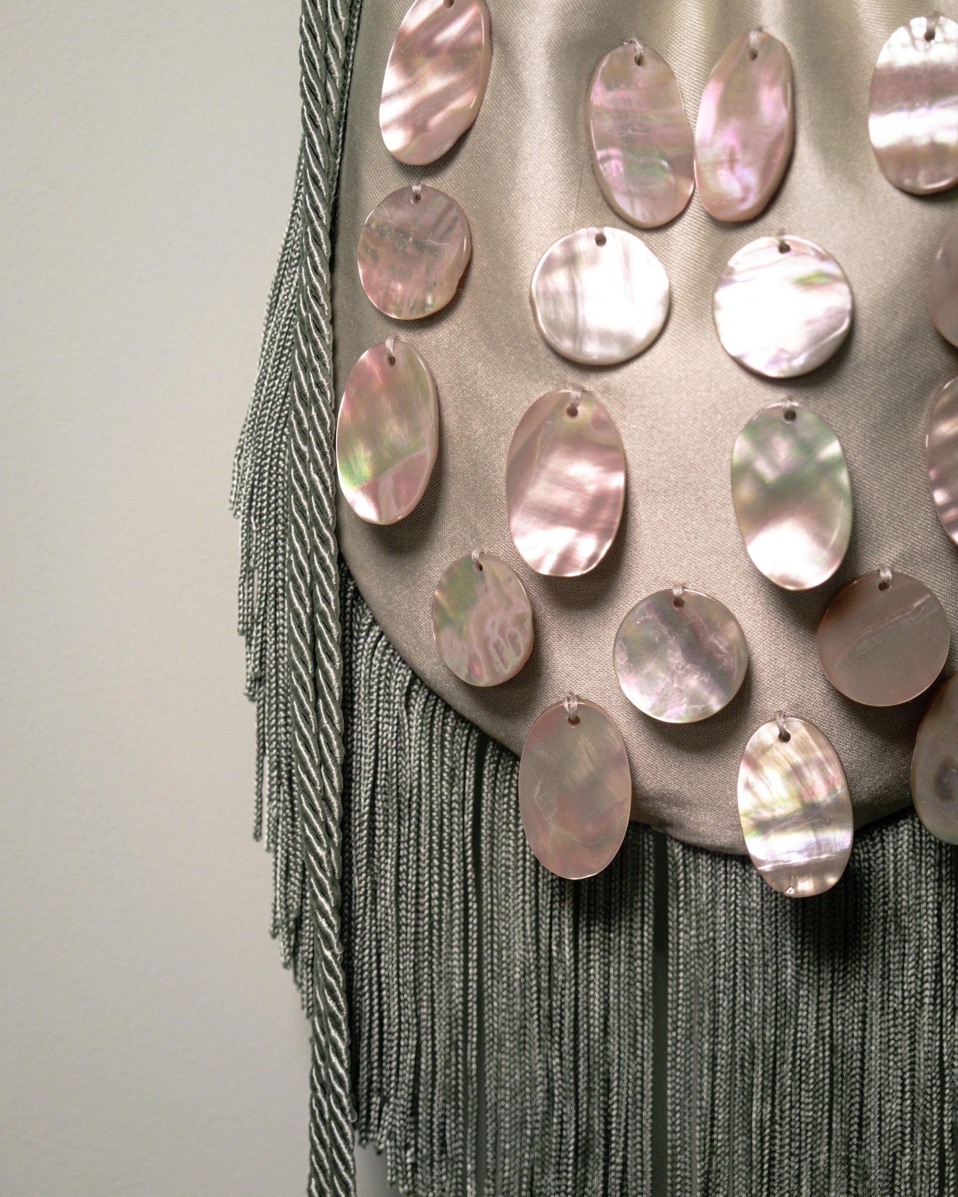 Close-up of the decorative fringe trim and natural mother-of-pearl embellishments on the sage green reticule bag.