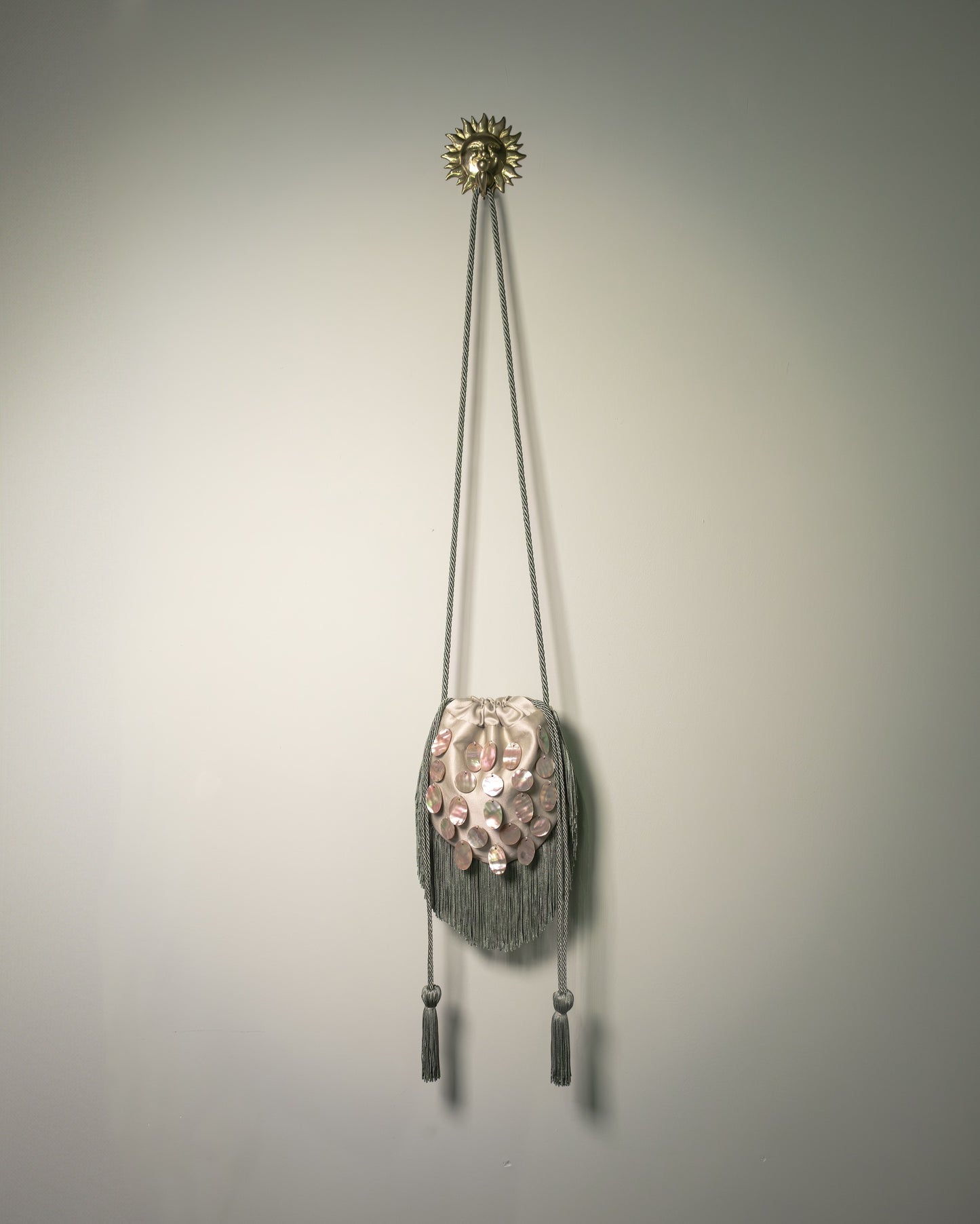 Sage green duchesse cotton reticule bag with hand-applied natural mother-of-pearl discs, decorative fringe and drawstring closure.