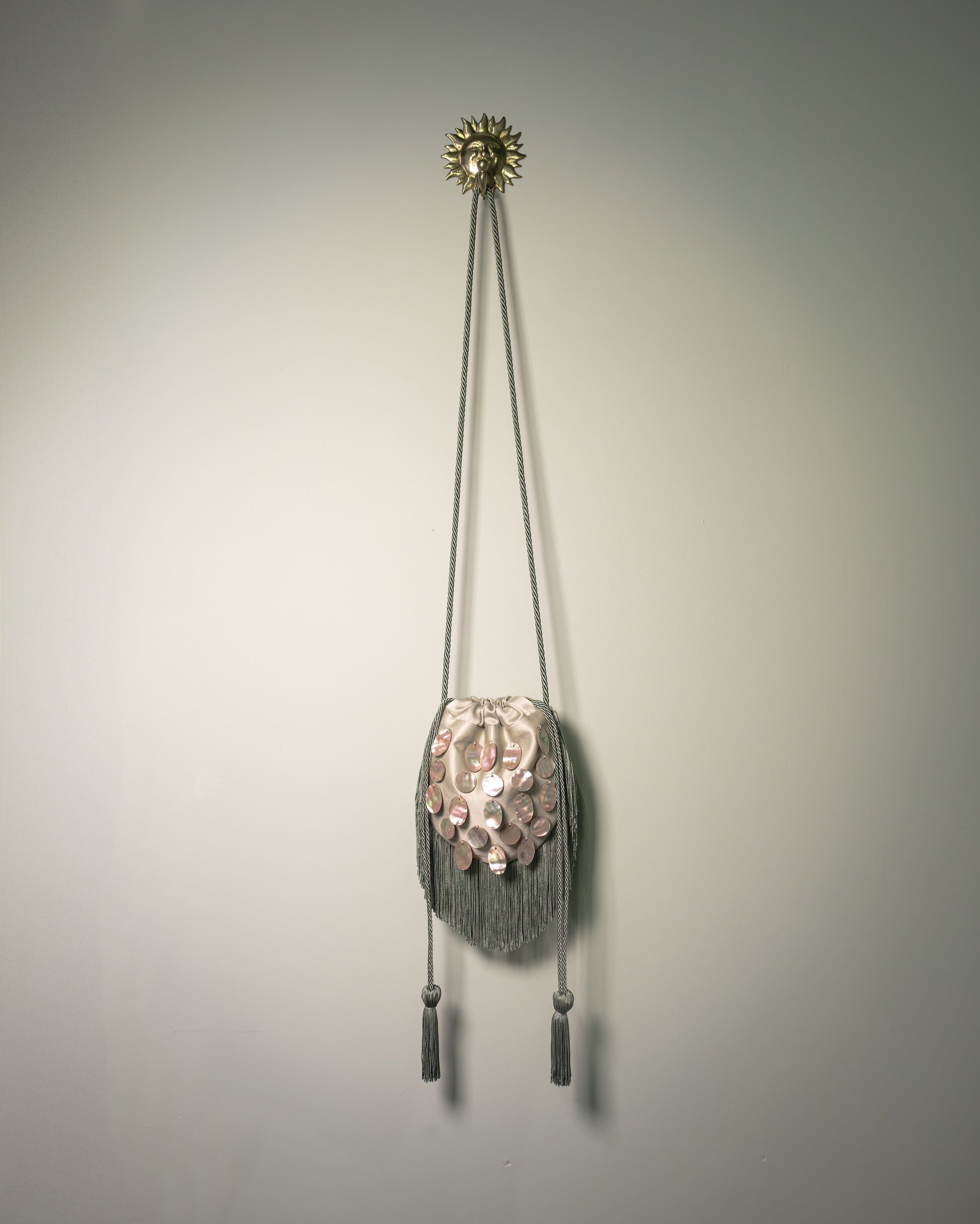 Sage green duchesse cotton reticule bag with hand-applied natural mother-of-pearl discs, decorative fringe and drawstring closure.