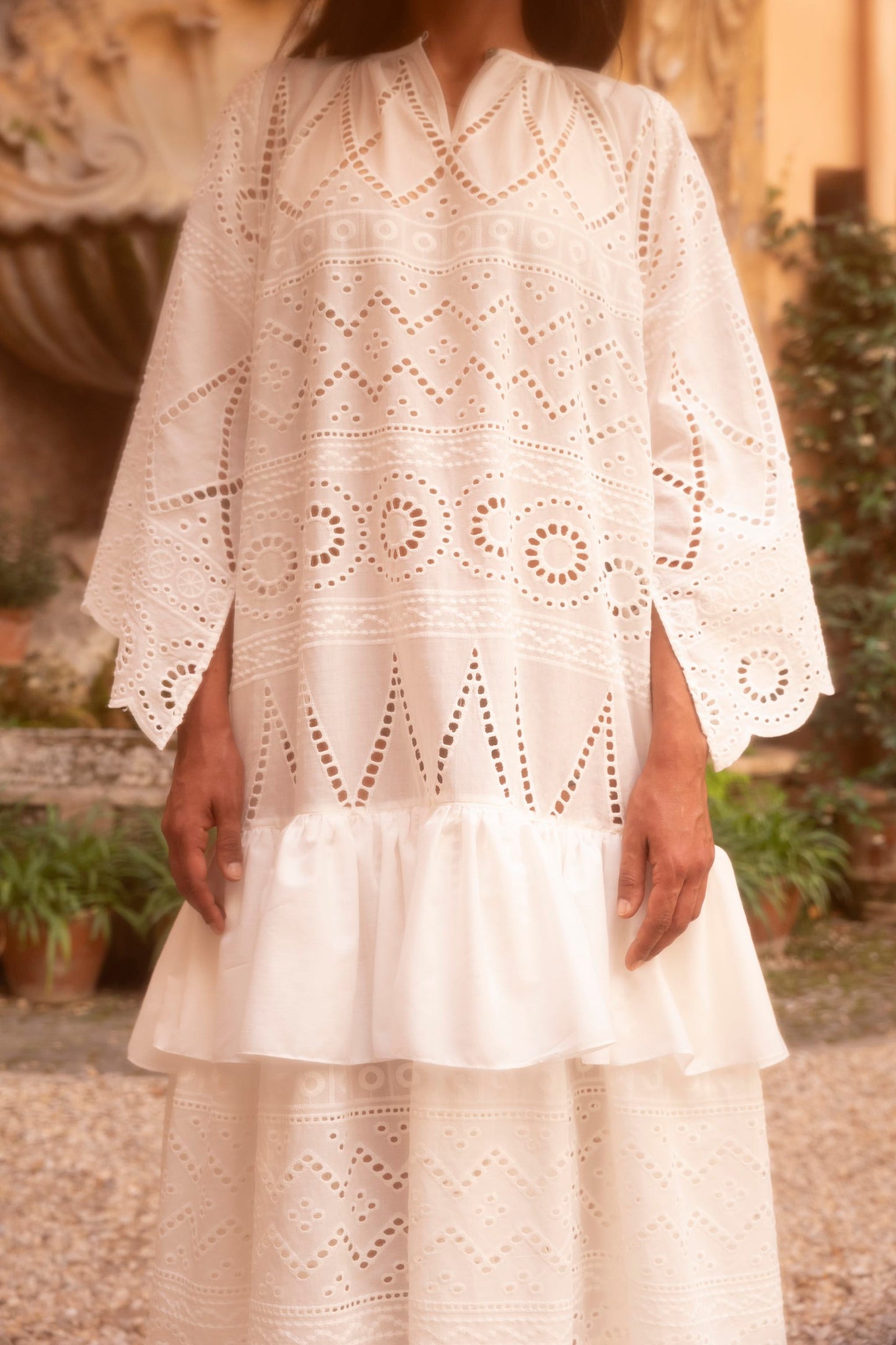 Detail of a broderie anglaise cotton batiste dress featuring geometric openwork embroidery, stand collar and wide sleeves.