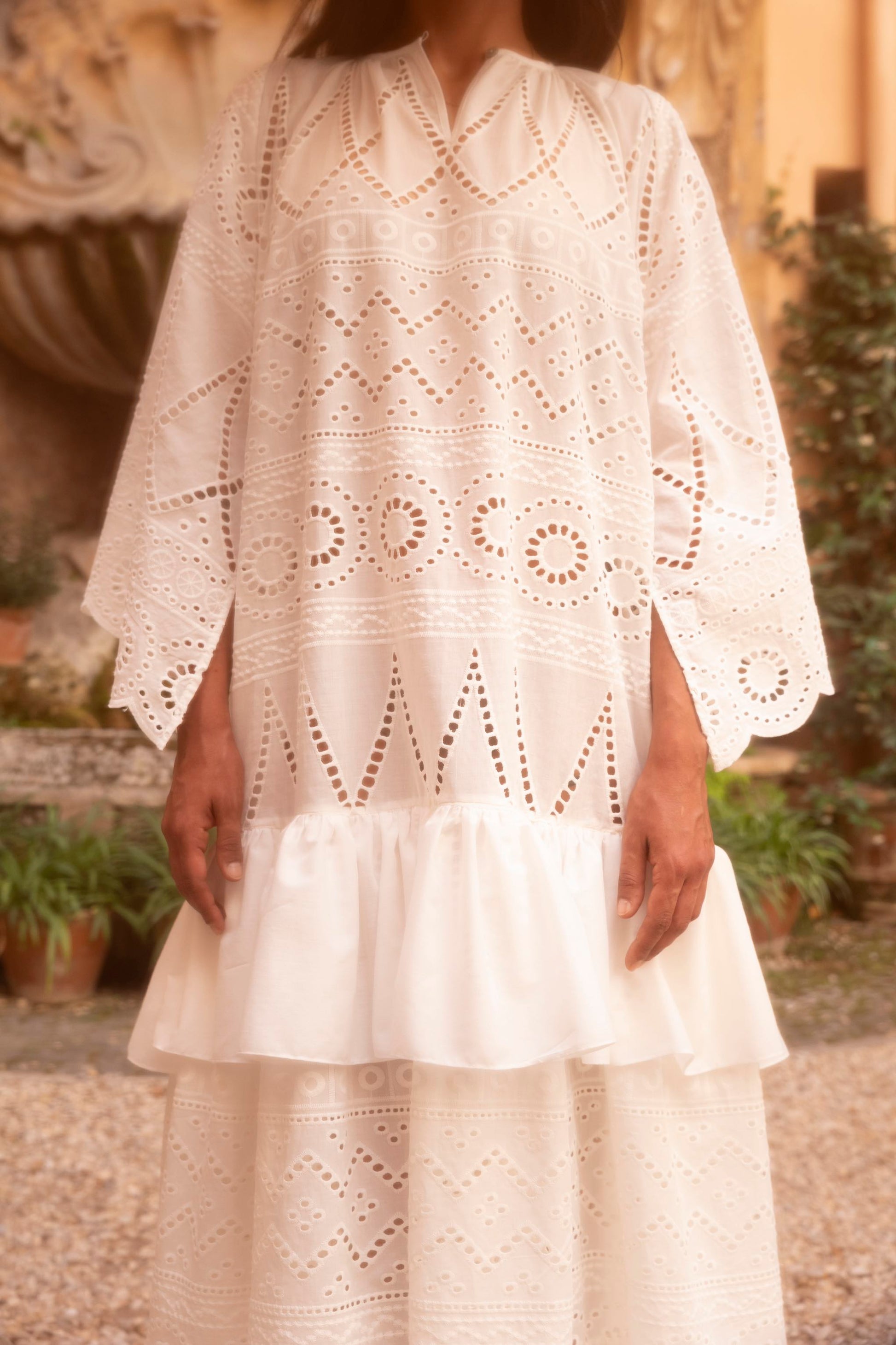Detail of a broderie anglaise cotton batiste dress featuring geometric openwork embroidery, stand collar and wide sleeves.