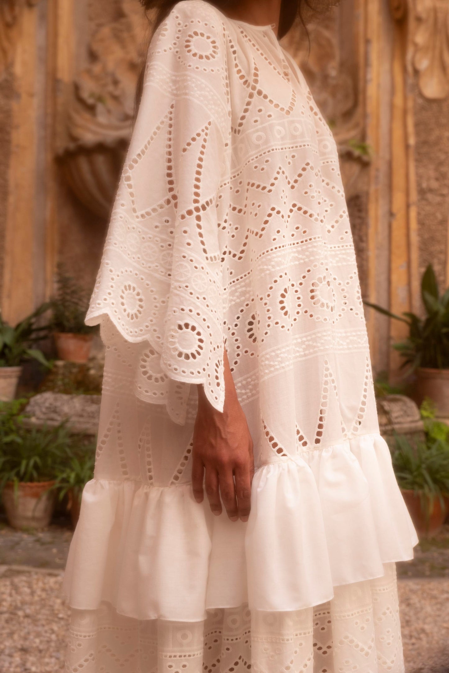 Side detail of a broderie anglaise cotton batiste dress with wide sleeves, geometric embroidery and gathered cotton voile tiers.
