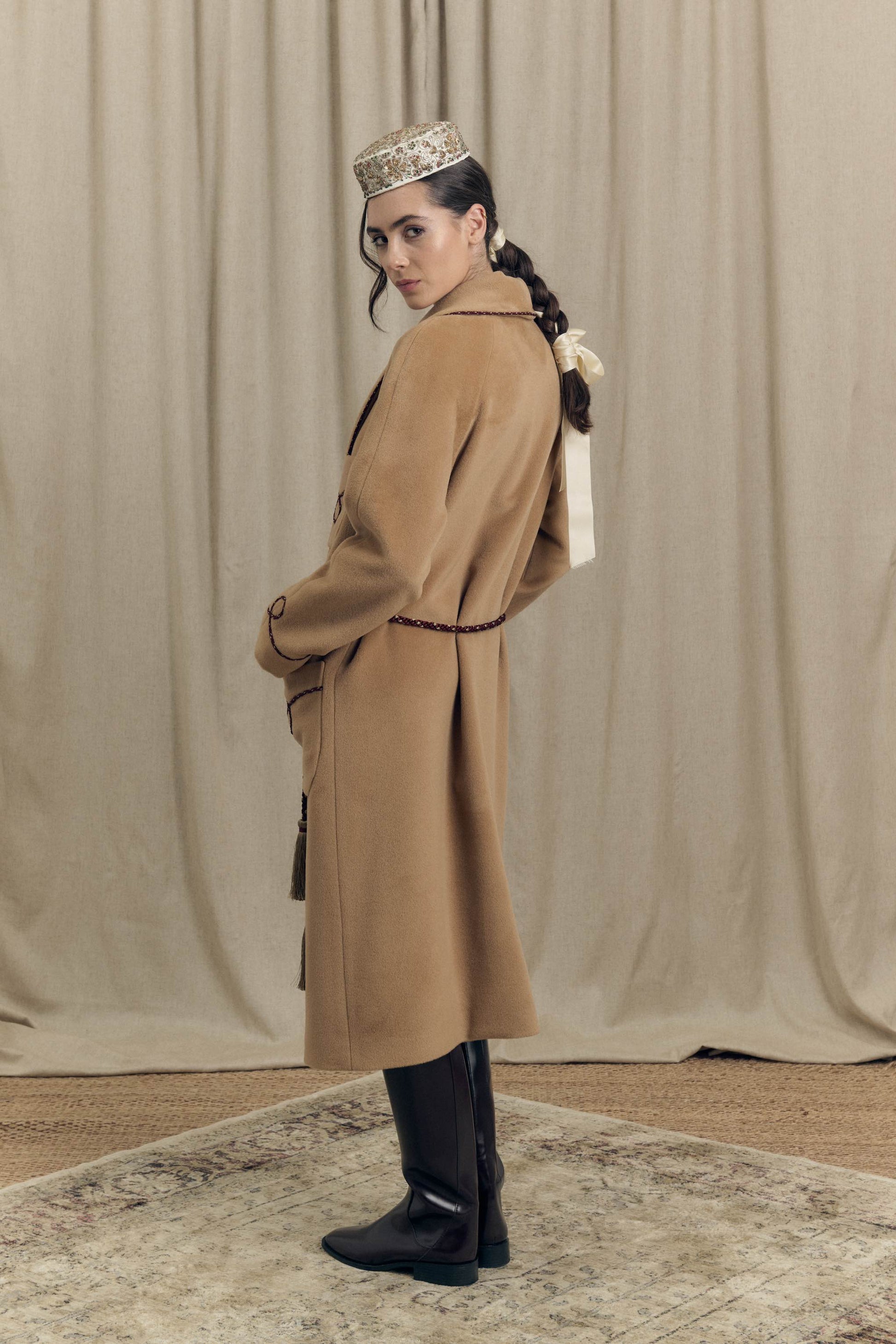 Back view of camel combed wool wrap coat featuring a perlé cord belt and clean wrap construction, Botteghe Oscure lookbook.
