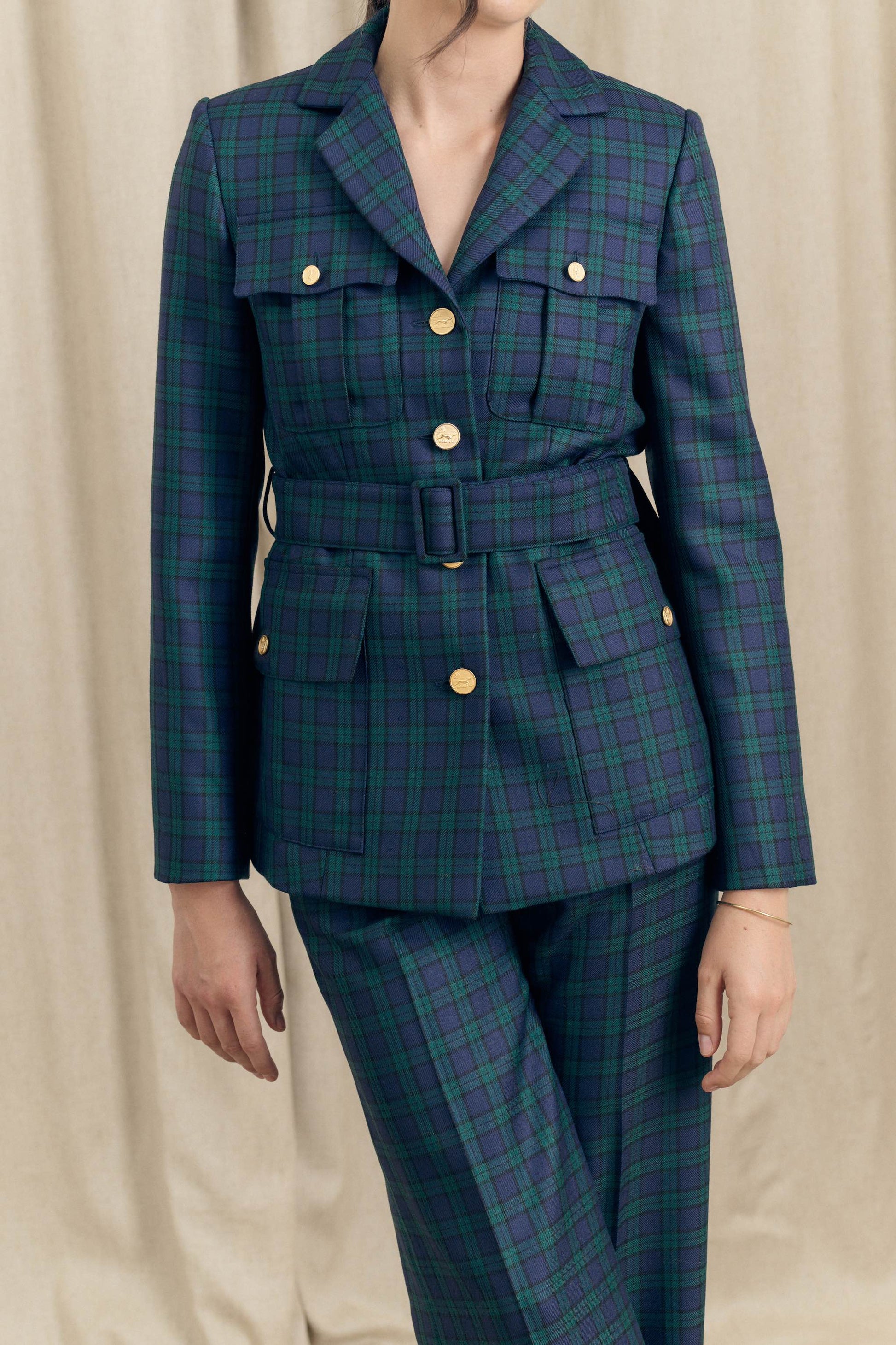 Close torso view of belted military blazer in Black Watch tartan wool with gold buttons and flap pockets by Botteghe Oscure.