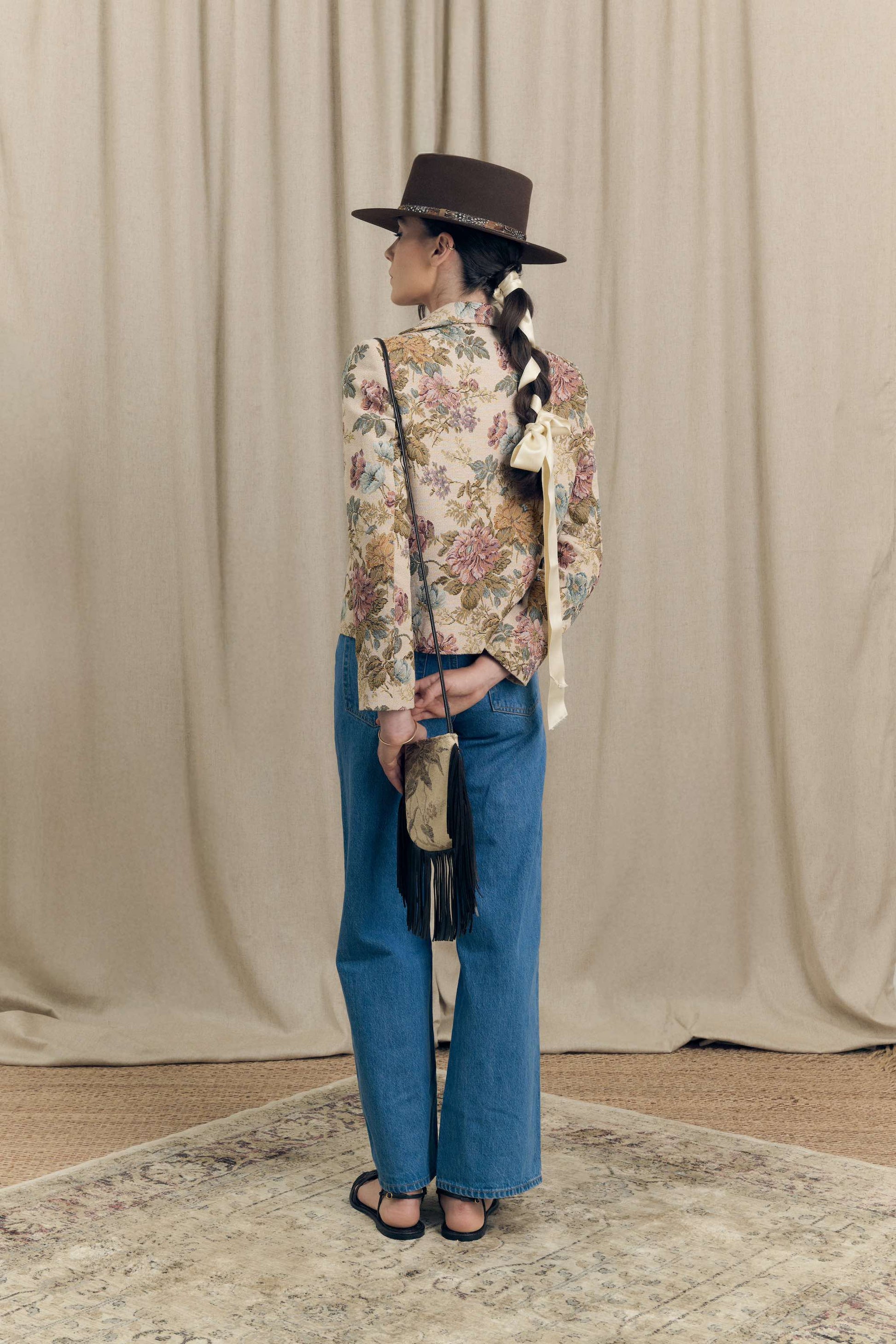Back view of floral vintage jacquard blazer by Botteghe Oscure, boxy fit with tailored cut, styled with crossbody mini bag in tapestry fabric and leather fringes.