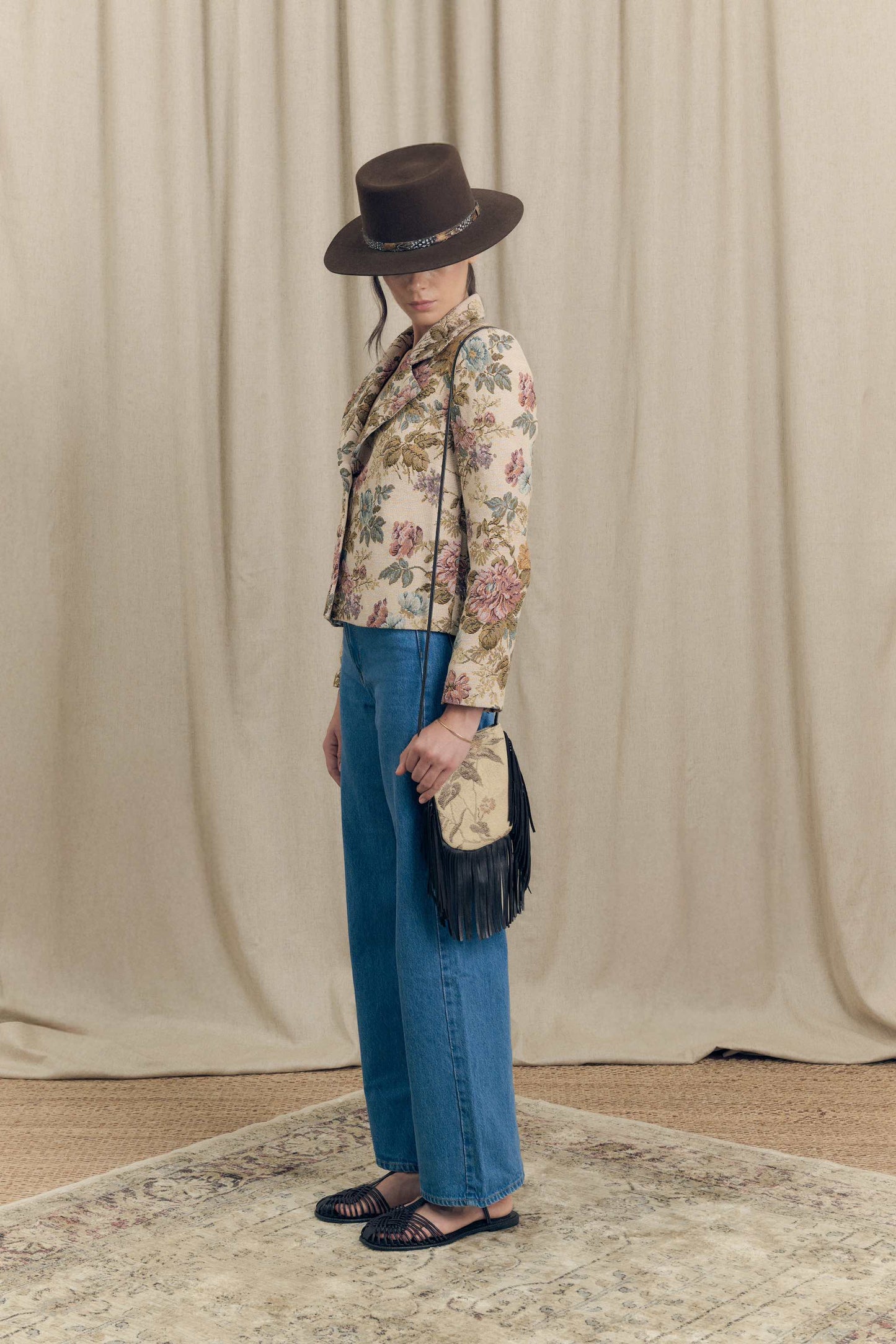 Side view of floral jacquard blazer by Botteghe Oscure with structured shoulders, vintage tapestry pattern and crossbody mini bag with leather fringes.