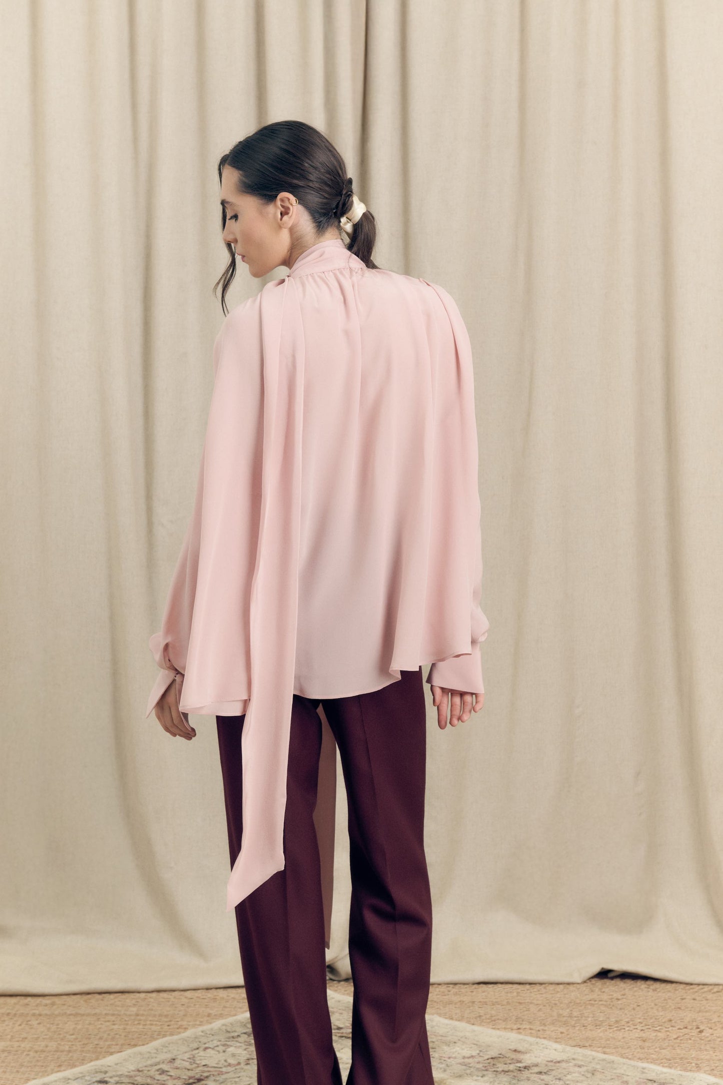 Back view of model wearing silk crepe de chine blouse with lavallière bow and ruched shoulders in blush pink by Botteghe Oscure