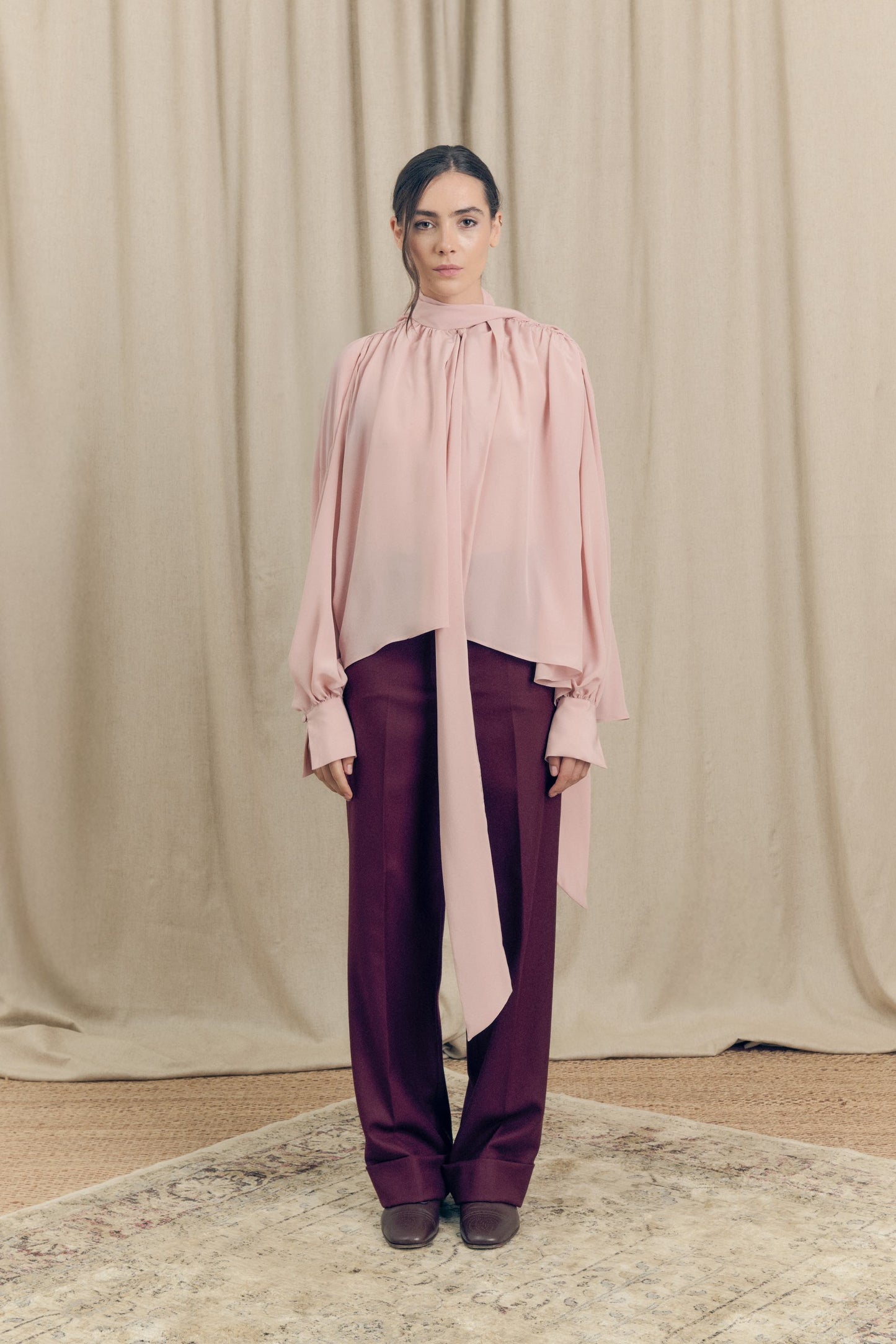 Front view of model wearing silk crepe de chine blouse with lavallière bow and ruched shoulders in blush pink by Botteghe Oscure