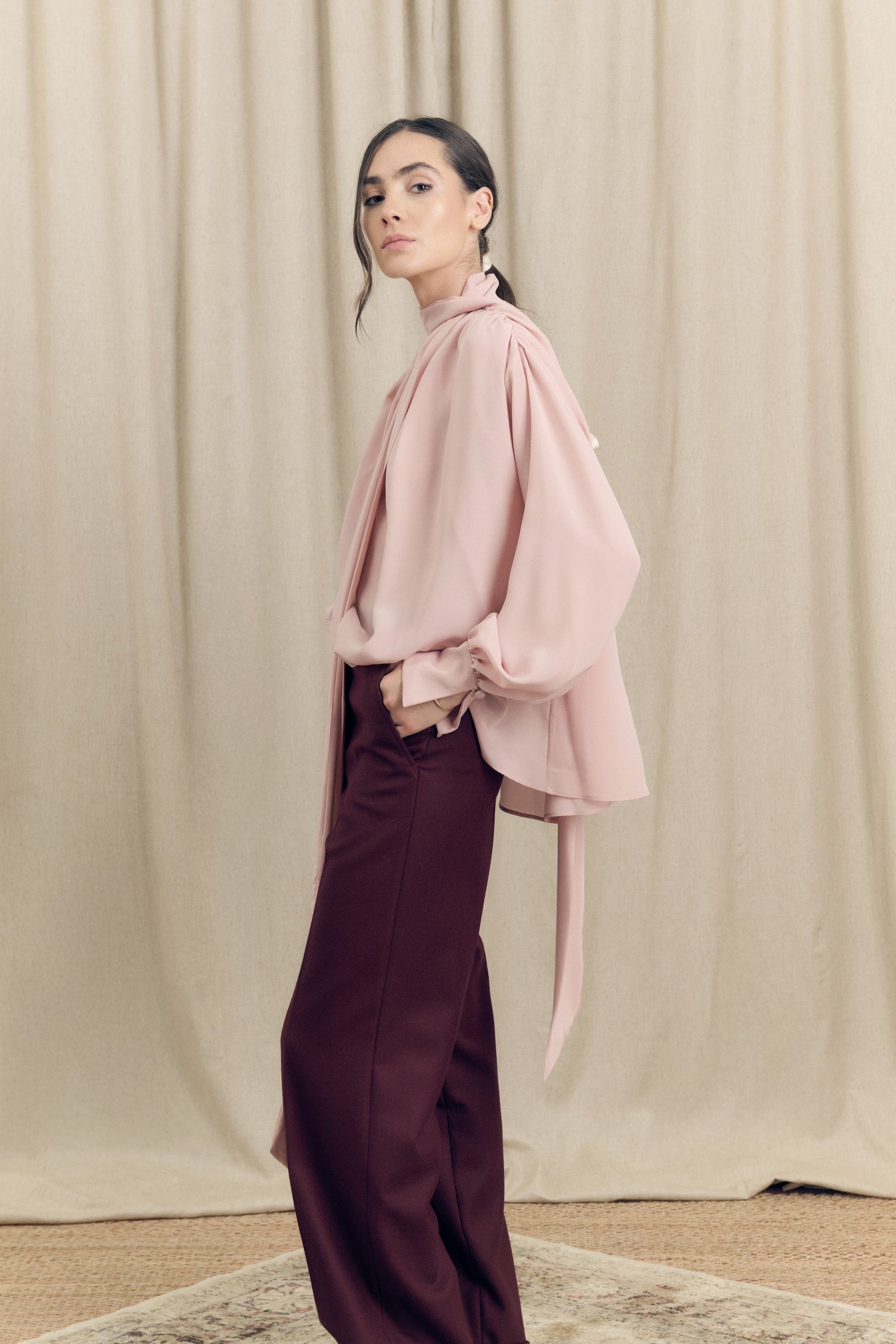 side view of model wearing silk crepe de chine blouse with lavallière bow and ruched shoulders in blush pink by Botteghe Oscure