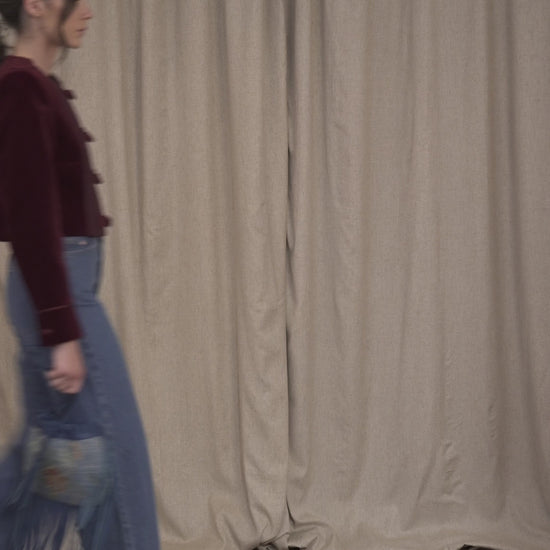 Model walking while wearing the Botteghe Oscure Brandebourg jacket in bordeaux velvet, featuring handcrafted braided frog closures, cropped boxy silhouette.