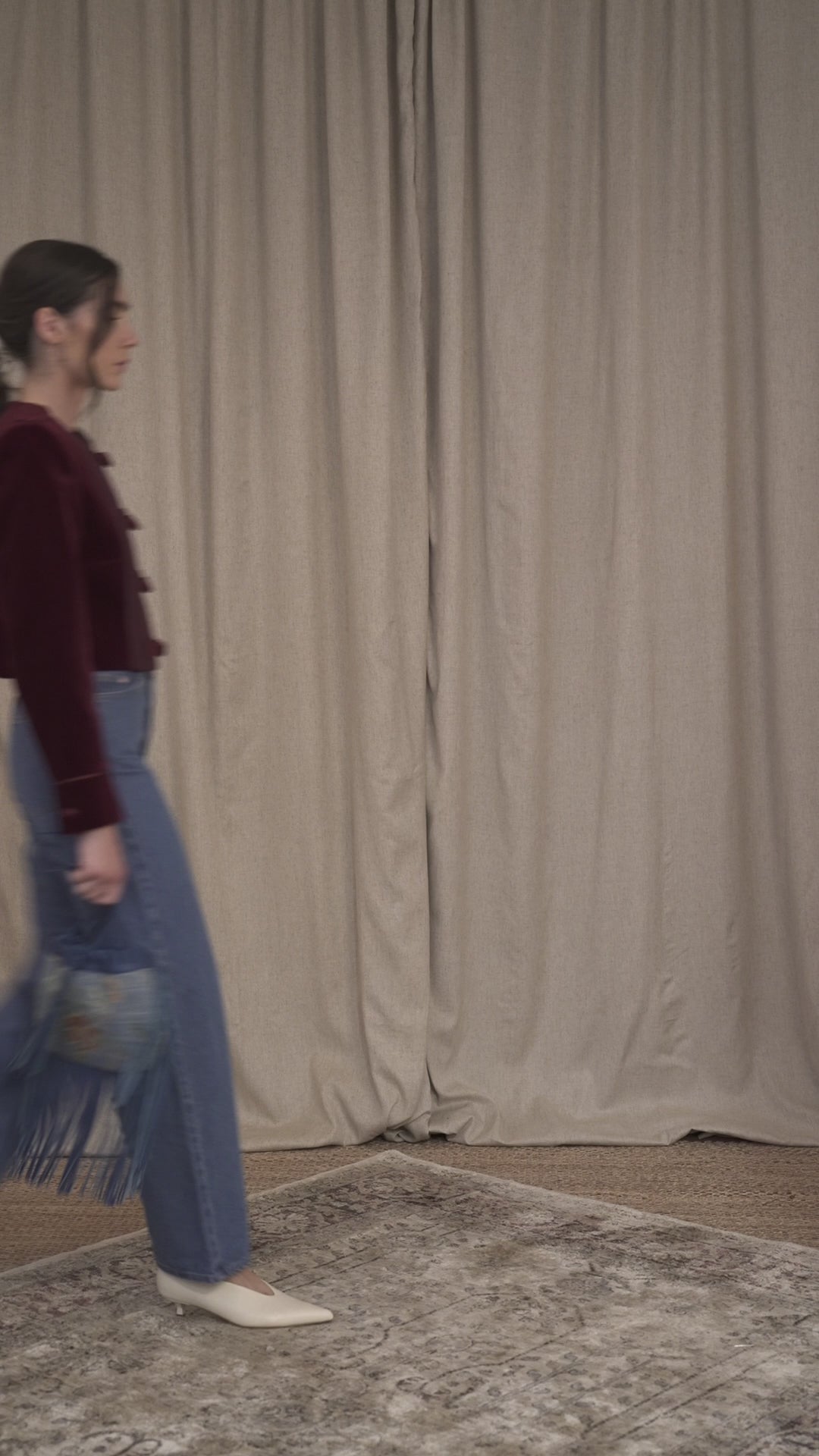 Model walking while wearing the Botteghe Oscure Brandebourg jacket in bordeaux velvet, featuring handcrafted braided frog closures, cropped boxy silhouette.