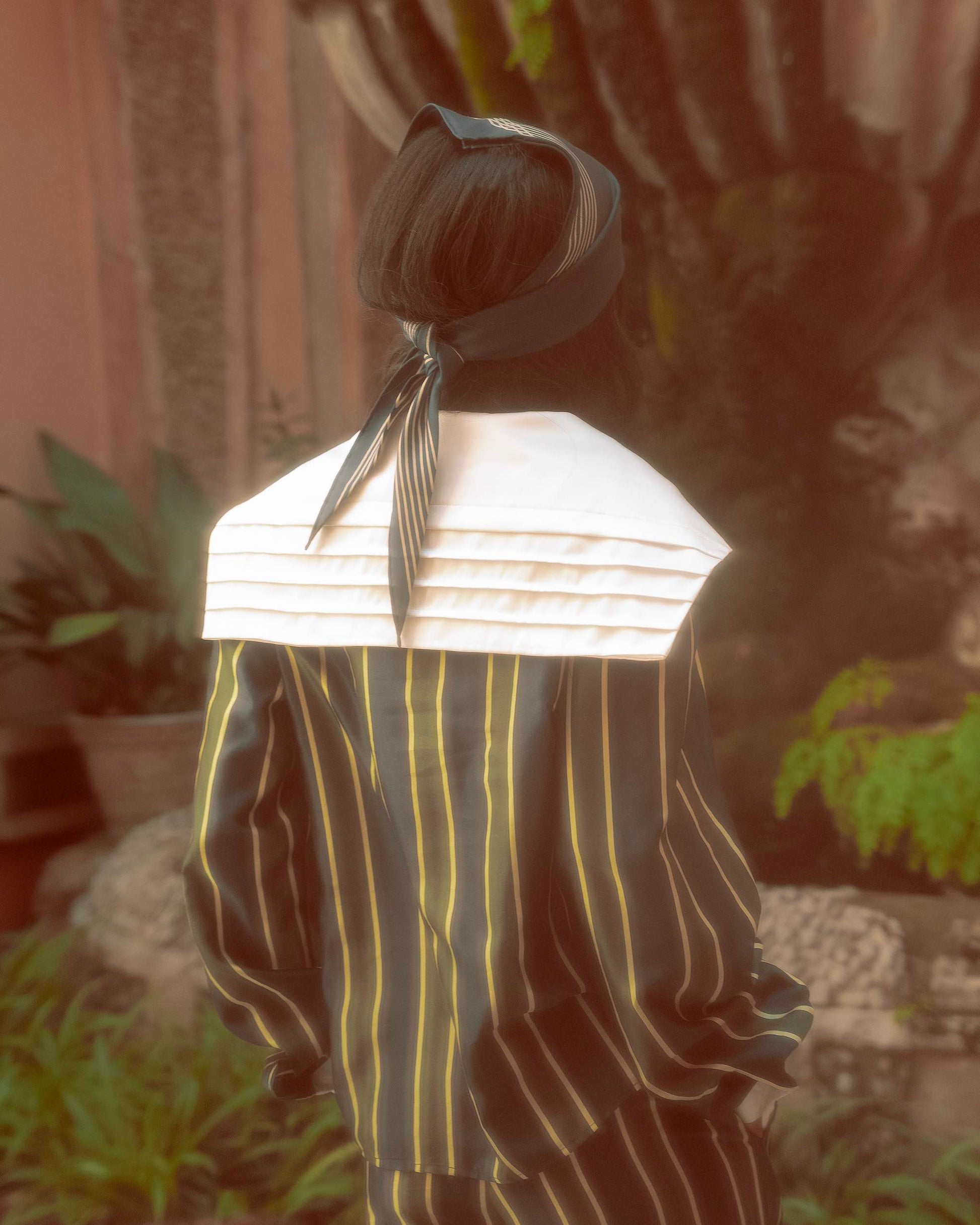 Model wearing oversized sailor shirt by botteghe Oscure in cotton and silk blend with a large silk pleated collar, back detail view.