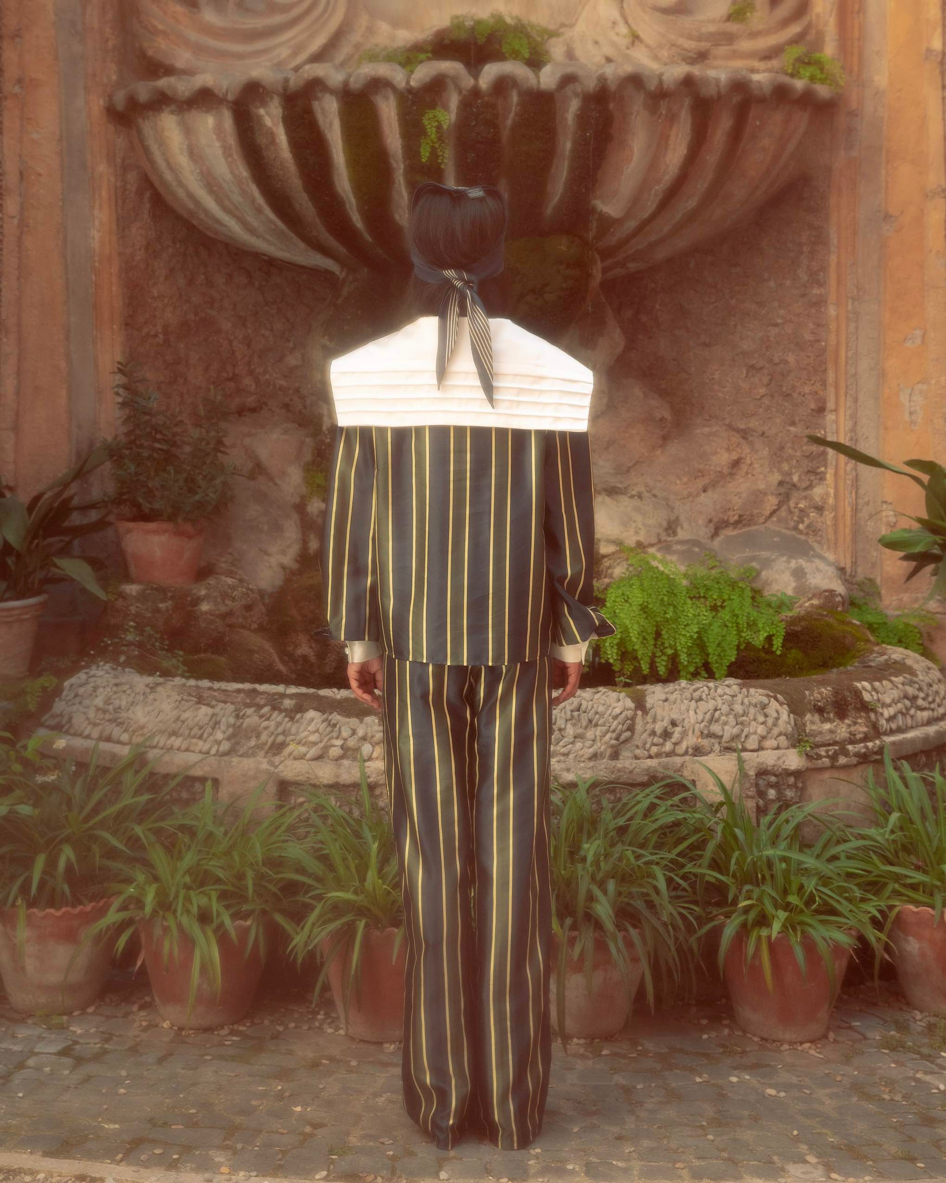 Model wearing oversized sailor shirt by botteghe Oscure in cotton and silk blend with a large silk pleated collar, back view.